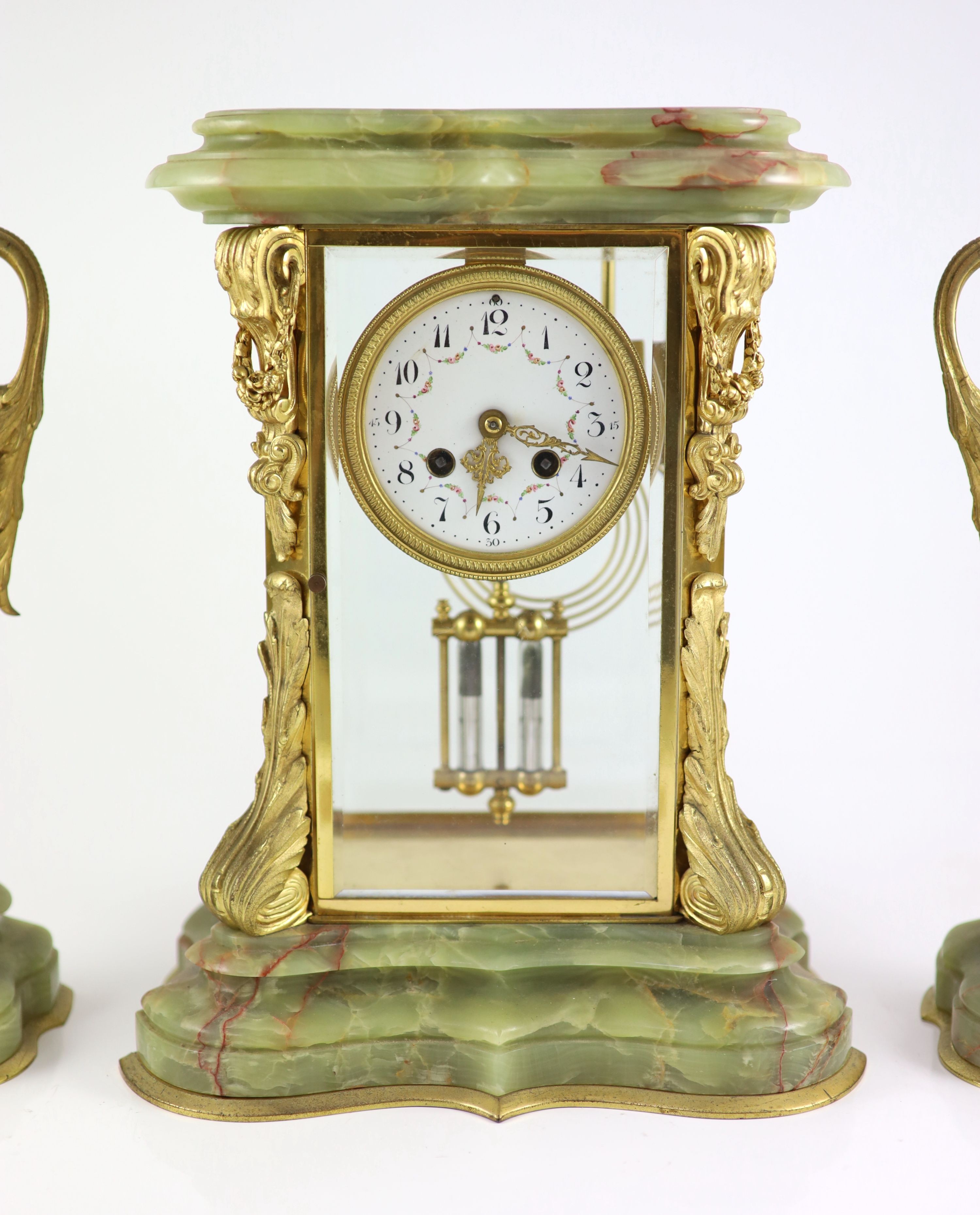 A green onyx and gilt metal clock garniture, comprising a four-glass regulator with enamelled dial in serpentine case and a pair of pedestal urns and covers Clock H 35cm. W 27cm. Urns H 36cm.
